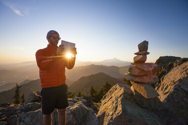 Ein Wanderer macht mit einem Tablet ein Foto von einem Steinhaufen auf dem Gipfel des Sauk Mountain. - AURF03692