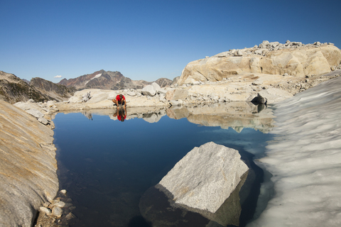 Ein Wanderer hält an, um aus einem von einem Gletscher gespeisten Bergsee in der Nähe von Whistler, British Columbia, Kanada, zu trinken., lizenzfreies Stockfoto