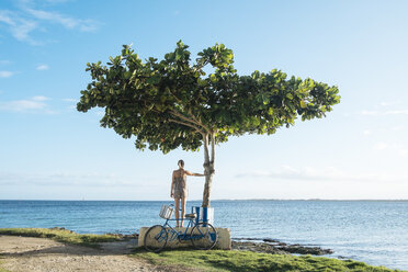 A girl stands with her bike next to a tree in Playa Larga, Cuba - AURF03707