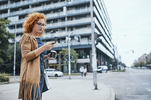 Junge Frau, die darauf wartet, die Straße zu überqueren, und ein Smartphone benutzt - ZEDF01514