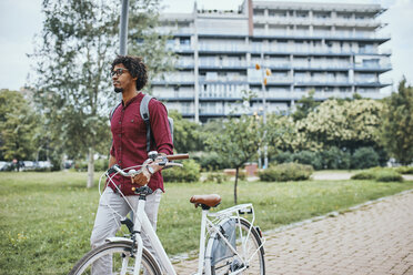 Young man with backpack pushing bicycle in park - ZEDF01538