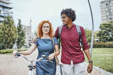 Friends walking in park, talking, woman pushing bicycle - ZEDF01541