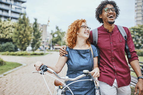 Freunde gehen im Park spazieren, unterhalten sich, Frau schiebt Fahrrad, lizenzfreies Stockfoto