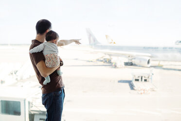Spain, Barcelona, Man holding a baby girl at the airport pointing at the airplanes - GEMF02399