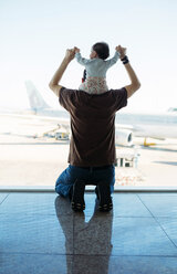 Man carrying a baby girl on his shoulders at the airport and looking at the airplanes, rear view - GEMF02401