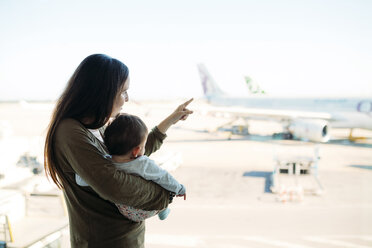 Mutter hält ein kleines Mädchen auf dem Flughafen, das auf die Flugzeuge zeigt - GEMF02402