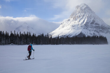 Eine Frau fährt auf dem Two Medicine Lake vor dem Sinopah Mountain und dem Painted Tepee Peak im Glacier National Park, Montana, Ski. - AURF03799