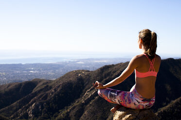 Eine Frau in einer bunten Hose sitzt mit gekreuzten Beinen auf dem Lower Gibraltar Rock in Santa Barbara, Kalifornien. Der Lower Gibraltar Rock bietet eine großartige Aussicht auf Santa Barbara und den Pazifischen Ozean. - AURF03849