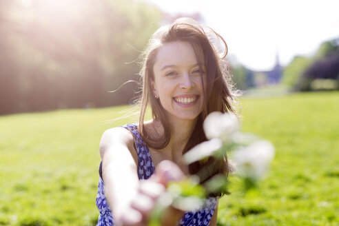 Porträt einer lächelnden jungen Frau in einem Park mit Blumen - GIOF04282