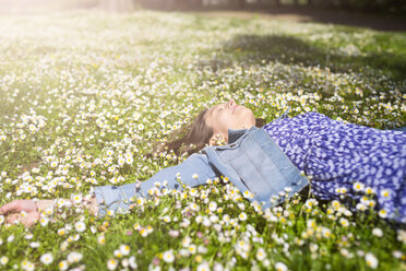 Relaxed young woman lying on flower meadow in a park - GIOF04283