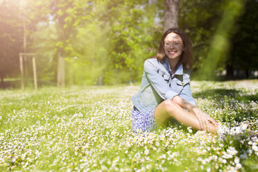 Smiling young woman sitting in a park - GIOF04284