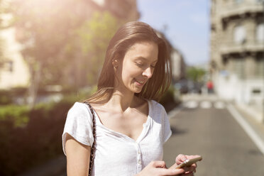 Lächelnde junge Frau mit Blick auf das Handy in der Stadt - GIOF04290