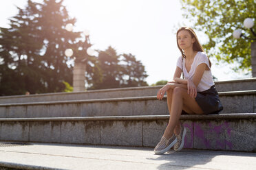Lächelnde junge Frau sitzt auf einer Treppe in der Stadt - GIOF04293