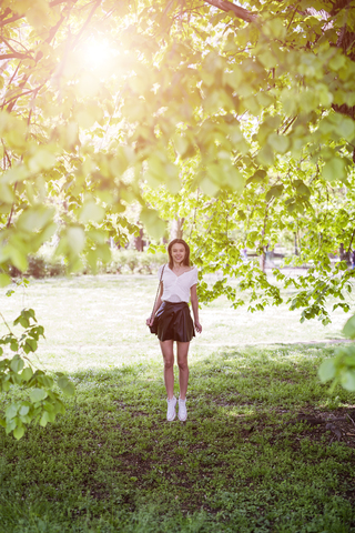 Lächelnde junge Frau in einem Park stehend, lizenzfreies Stockfoto