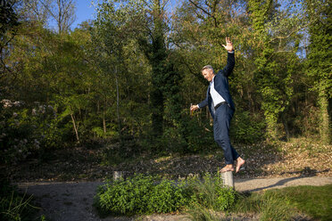 Businessman balancing barefoot on pole in nature - FMKF05229