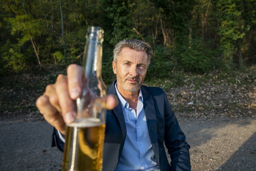 Portrait of mature businessman toasting with beer in nature - FMKF05234