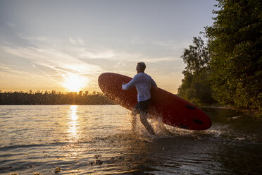 Mann mit Paddelbrett zu Fuß in den See bei Sonnenuntergang - FMKF05237