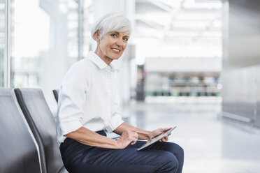 Smiling senior businesswoman sitting in waiting area using tablet - DIGF05017