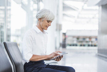 Ältere Geschäftsfrau sitzt im Wartebereich und benutzt ein Tablet - DIGF05018