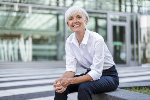 Porträt einer lächelnden älteren Geschäftsfrau, die draußen sitzt, lizenzfreies Stockfoto