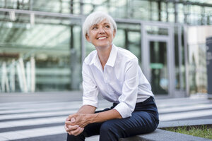 Lächelnde ältere Geschäftsfrau, die draußen sitzt und sich umschaut - DIGF05035