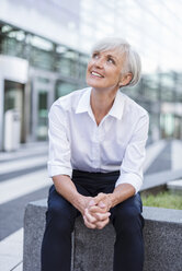 Lächelnde ältere Geschäftsfrau, die draußen sitzt und nach oben schaut - DIGF05036