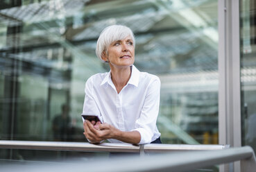 Senior businesswoman leaning on railing in the city with cell phone - DIGF05047