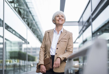 Smiling senior businesswoman leaning on railing in the city looking up - DIGF05051