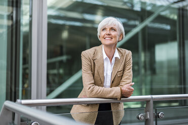 Portrait of smiling senior businesswoman leaning on railing in the city looking up - DIGF05054