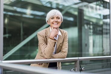 Porträt einer lächelnden älteren Geschäftsfrau, die sich auf ein Geländer in der Stadt stützt - DIGF05055
