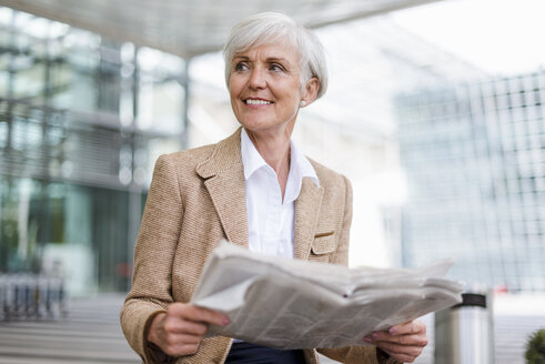 Lächelnde ältere Geschäftsfrau mit Zeitung in der Stadt sitzend - DIGF05062