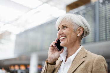 Lächelnde ältere Geschäftsfrau am Mobiltelefon auf dem Flughafen - DIGF05066