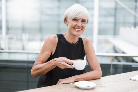 Porträt einer lächelnden älteren Frau, die einen Kaffee trinkt, lizenzfreies Stockfoto