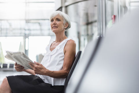 Ältere Frau sitzt im Wartebereich mit Zeitung, lizenzfreies Stockfoto