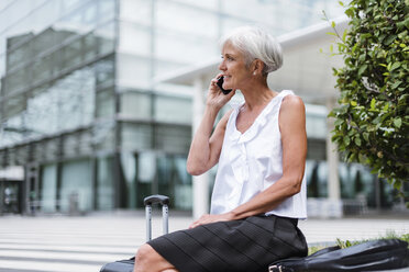 Smiling senior woman with baggage on cell phone in the city - DIGF05090