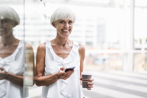 Porträt einer lächelnden älteren Frau mit Mobiltelefon und Mitnahmekaffee im Freien - DIGF05098