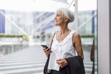 Ältere Frau mit Mobiltelefon in der Stadt, die sich umschaut - DIGF05102