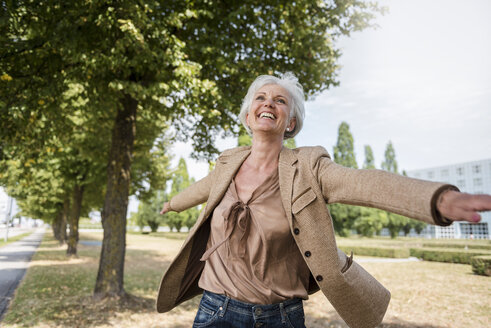 Happy senior woman with outstretched arms in a park - DIGF05114