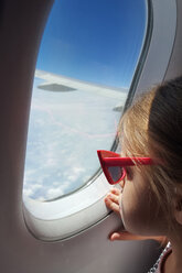 Mädchen schaut durch ein Fenster in einem fliegenden Flugzeug - AURF03988