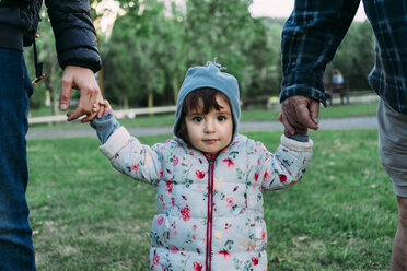 Porträt eines modischen kleinen Mädchens, das an der Hand seines Großvaters und seines Vaters durch einen Park geht - GEMF02407