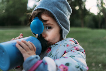 Porträt eines modischen kleinen Mädchens, das in einem Park Wasser trinkt - GEMF02409