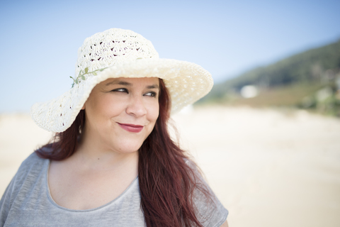 Porträt einer lächelnden Frau mit Sommerhut am Strand, lizenzfreies Stockfoto