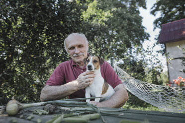 Älterer Mann sitzt mit Hund am Gartentisch - KMKF00529