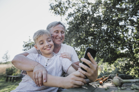 Glückliche Großmutter und Enkel machen ein Selfie im Garten, lizenzfreies Stockfoto