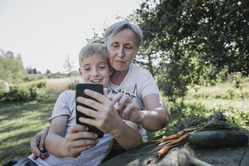 Grandmother and grandson taking a selfie in garden - KMKF00532