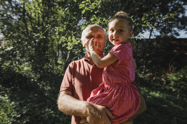 Grandfather carrying granddaughter in garden - KMKF00538