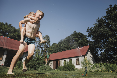 Bruder und Schwester spielen mit Gartenschlauch im Garten, lizenzfreies Stockfoto