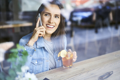 Lächelnde junge Frau am Telefon trinkt Tee in einem Café - BSZF00564