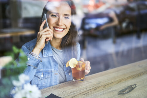 Lächelnde junge Frau am Telefon trinkt Tee in einem Café - BSZF00565