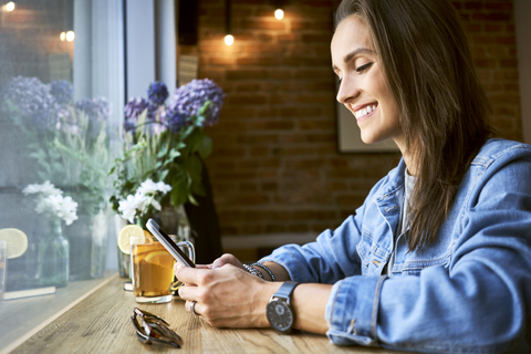 Smiling young woman using phone in cafe stock photo